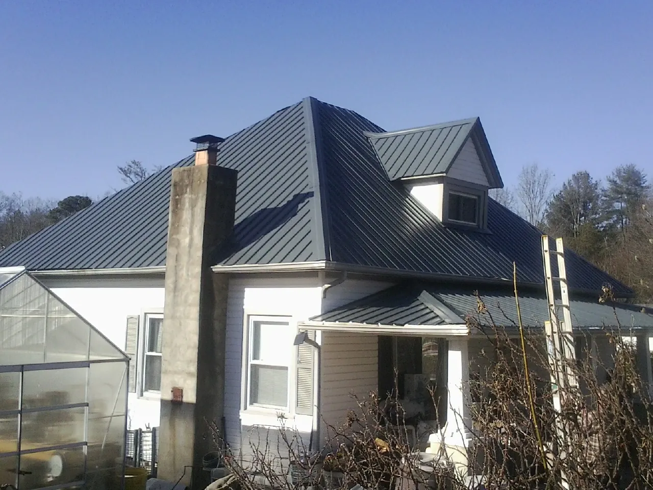 Dark blue standing seam metal roof on a white farmhouse with dormer — Slate & Tile Roof Repair by Roofing Brothers in Rolesville