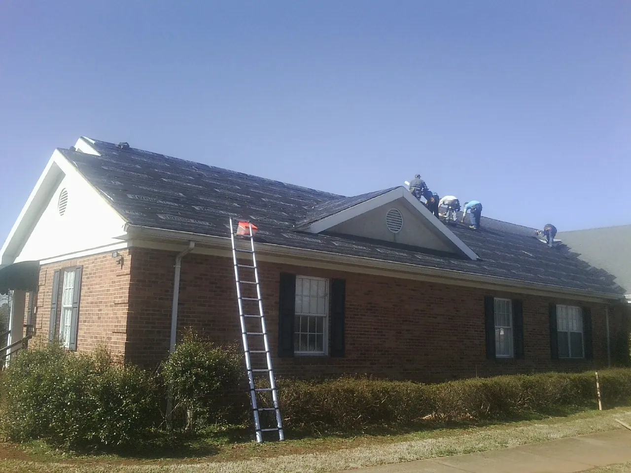 Crew tearing shingles off a brick ranch roof with a ladder set — Emergency Roof Repair work by our crew in Rolesville