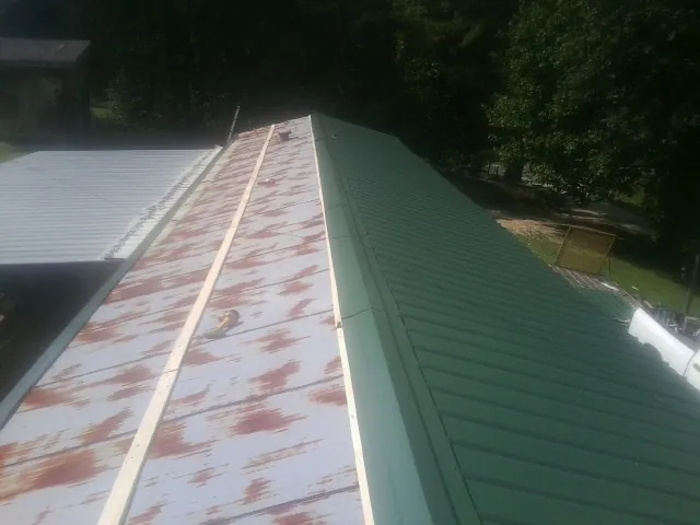 Old rusted panels beside newly installed green metal roofing — Wind Damage Roof Repair by Roofing Brothers in Rolesville