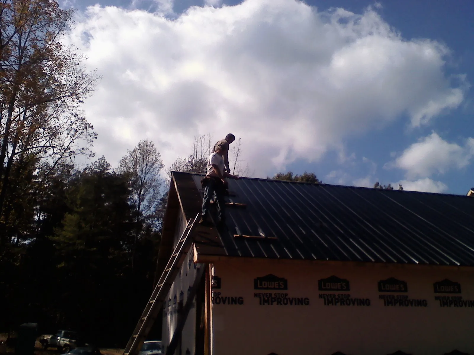 Roofer fastening dark metal panels high against a cloudy sky, from a Roof Inspection job in Rolesville