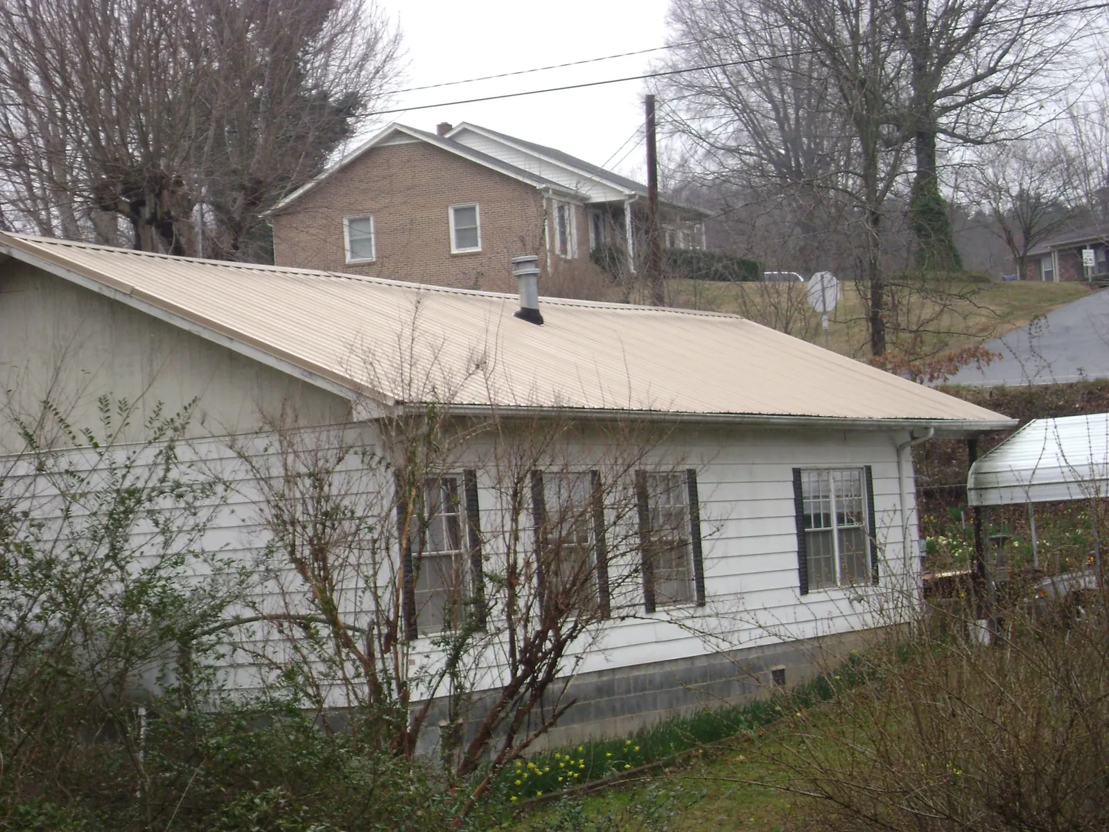 Tan metal roof on a white sided house set into a hillside — Commercial Roofing by Roofing Brothers in Rolesville