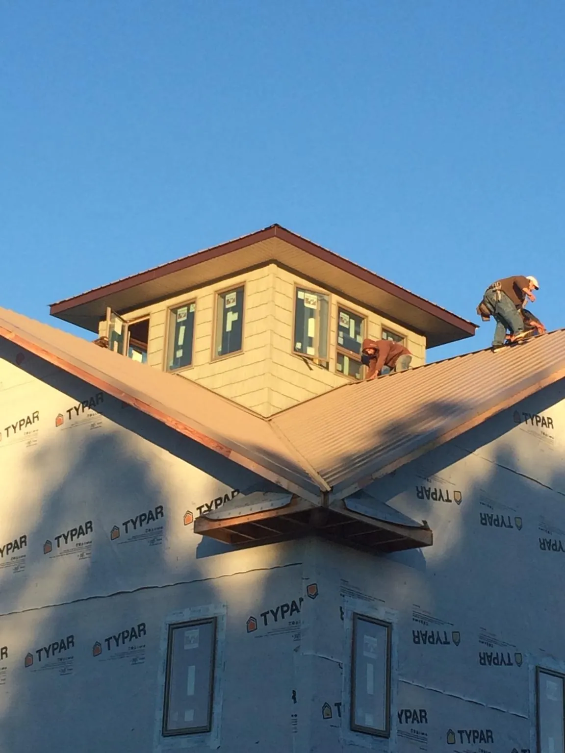 Roofers working around a rooftop cupola on a new metal roof at sunset — Roof Waterproofing in Rolesville by Roofing Brothers